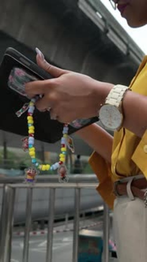 Black Asian Girl with Headphones in Her Ears Checks Her Tablet in the Center of a Big City