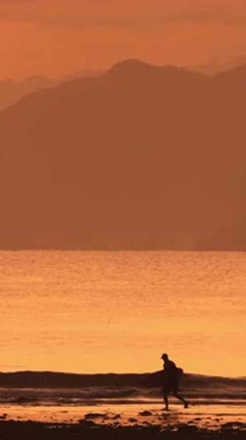 Silhouette of Surfer Walking on Beach at Sunset