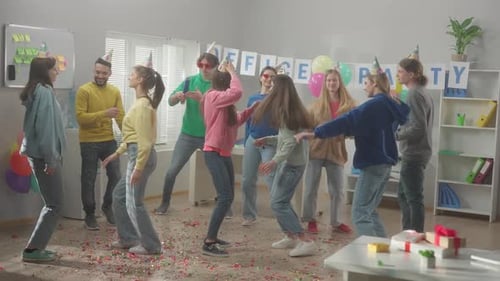 A Group of Colleagues in Festive Hats and Glasses are Dancing Having Fun Celebrating a Common