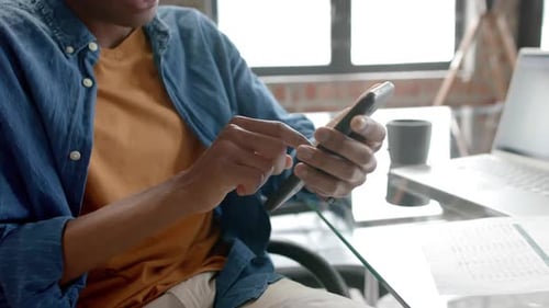 Midsection of african american casual businessman sitting using smartphone at home, slow motion