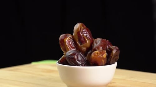 Dates fruits in bowl rotate on wooden background close up, rotation. Eating dried fruits. Vegan