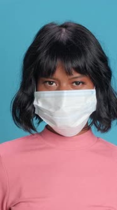 Woman in a Pink Sweater Wears a Mask Against a Vibrant Blue Background