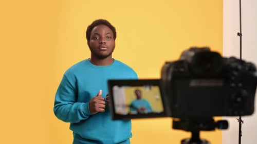 Blogger afroamericano graba un vídeo tutorial con cámara en un estudio con fondo naranja