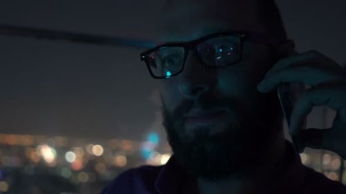 Young man chatting on cellphone enjoying cocktail at rooftop bar at night