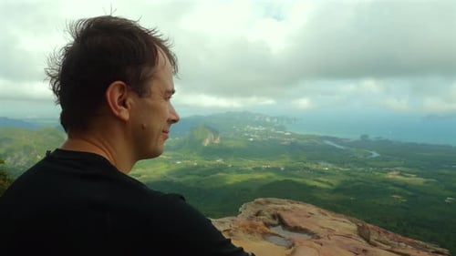Man Enjoying Scenic Overlook with Vast Green Landscape and Cloudy Sky