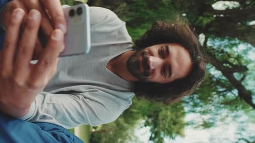 Young man using mobile phone while sitting on the lawn in the park