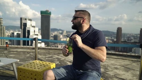 Man enjoying refreshing cocktail admiring city view from luxurious rooftop bar