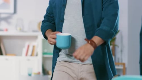 Anonymous Man Enters His Living Room with a Mug and Sits Down at His Desk Starts Working on a Lapto