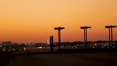 Airplane landing on runway at dusk with city skyline silhouette, golden sky backdrop