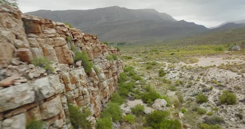 Drone flies close to a rock face towards a road where a black off-road vehicle is driving in Cederbe