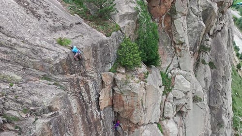 Climber Ascending Steep Rock Face with Belayer Below