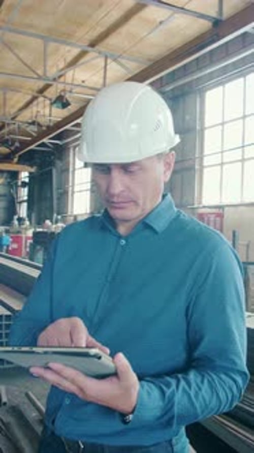 Man Using Tablet to Analyze Data Inside Industrial Workspace During Daytime