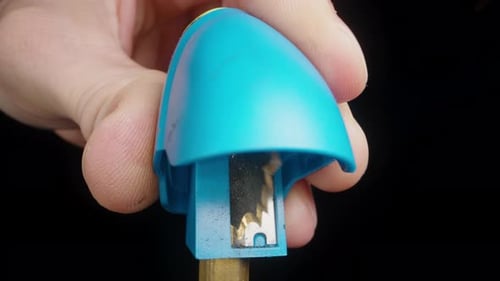 A man sharpens a pencil in a blue sharpener on a black background. Close-up.