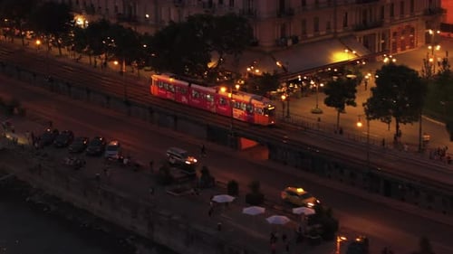 Tracking of Tram Driving in Streets of Evening City Illuminated Waterfront with Restaurants and