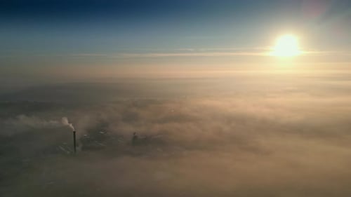 Smokestack Emitting Smoke Over Foggy Cityscape at Sunrise