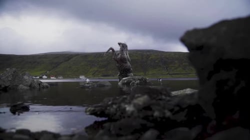 Low angle shot of horse statue standing in natural lake and hills in background during cloudy day.
