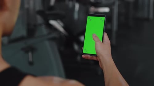 Young Male Athlete with a Sweaty Muscular Body in the Back View Uses a Sports App on His Smartphone