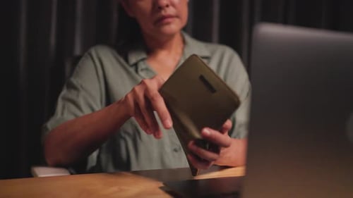 Woman takes money out of wallet and counts money to calculate spending while working on computer