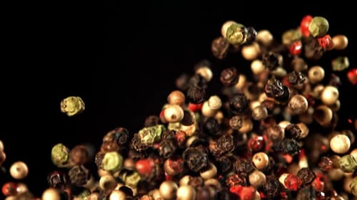 Mixed peppercorns falling in slow motion on black background