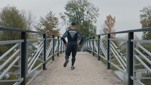 Active Man Jogging Away on a Metal Bridge in a Park with Autumn Trees Athlete Doing Cardio Training