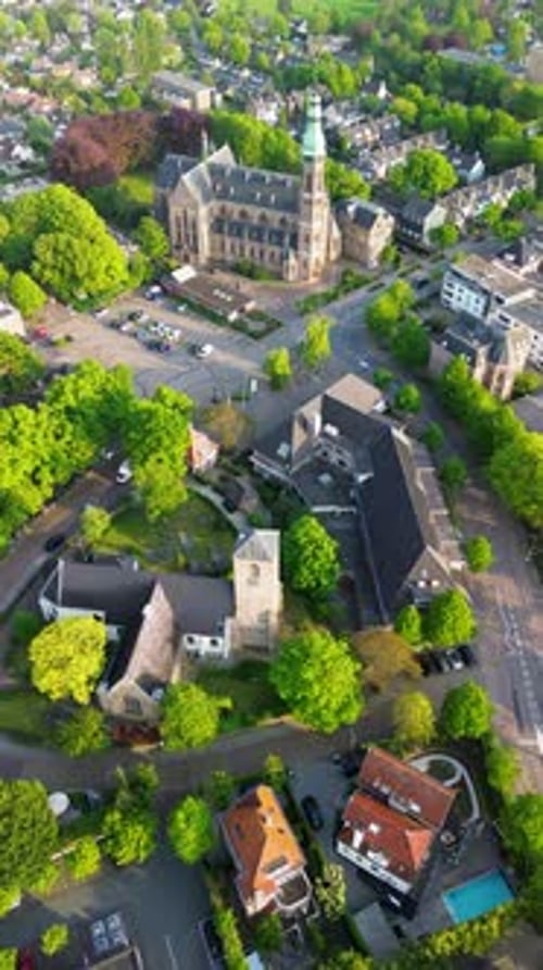 Aerial drone view of a town square with a parking lot, cars, trees, and geometric patterns
