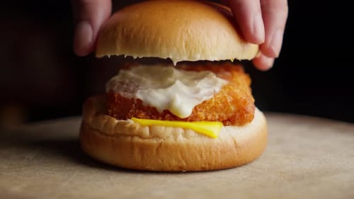 Putting Bun On Fried Fish Burger Spread With Mayonnaise And Cheese. Close-up Shot