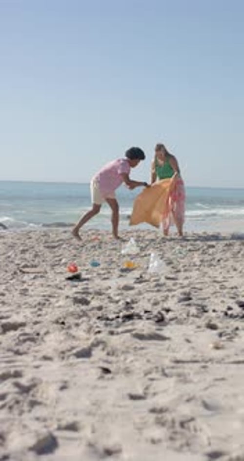 Vertical video: Cleaning beach, group of friends picking up trash from sand near ocean