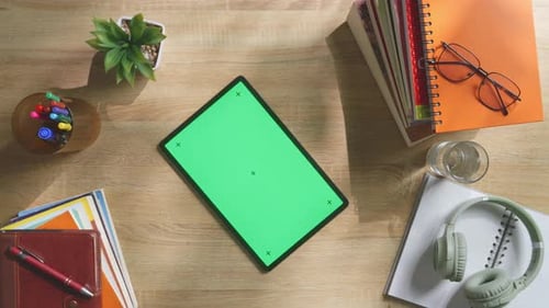 Top down view of a tablet with mock up green screen on a wooden desk