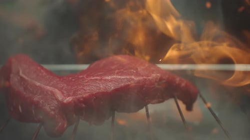 Grilled Meat Steak on Stainless Grill Depot with Fire on Dark Background Preparing Tasty Raw Red