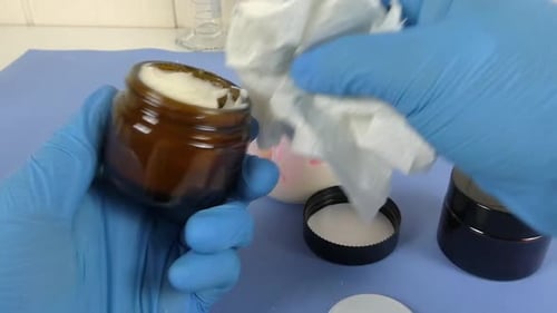 vue d'une scène de laboratoire de cosmétiques où un opérateur ganté utilise une spatule pour emballer soigneusement un sachet