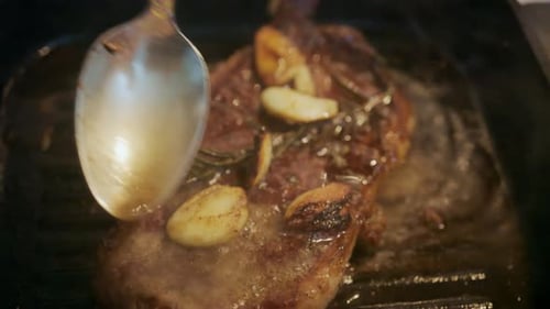 Close up of a juicy steak sizzling in a grill pan while being pressed with a spatula