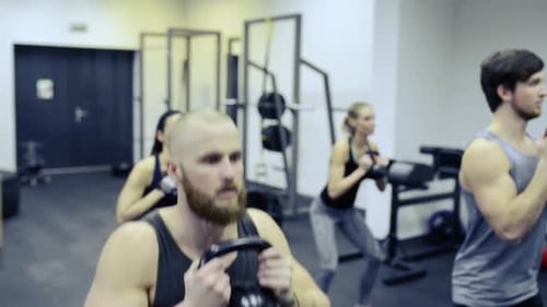 Young People in Gym Doing Squats with Kettlebells Active