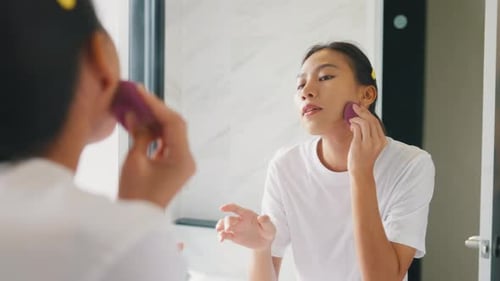 Woman Applies Makeup in Bathroom Mirror