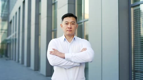 Portrait of a confident asian businessman in a shirt standing on the street near office building.