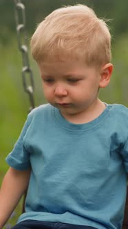 Sad Little Boy on a Swing in Park