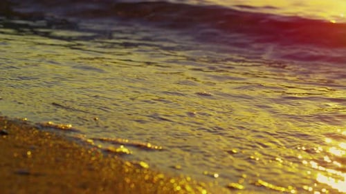 La luz dorada del sol se refleja en las olas del mar que salpican una hermosa playa de arena al atardecer
