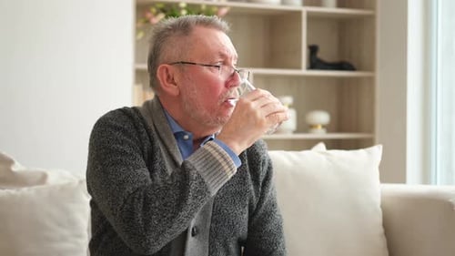 Alter Mann hält Glas in der Hand und trinkt zu Hause frisches Wasser, reifer alter älterer durstiger Großvater nimmt