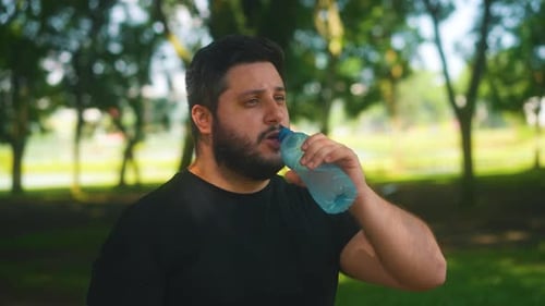 Bearded man drinking water after workout and running at the park being healthy and hydrated. Portrai
