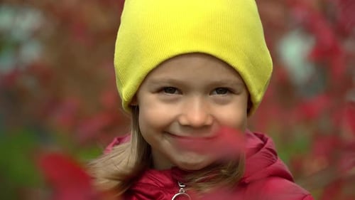 Happy Little Girl Looks at Camera and Smiles in Autumn Park in Wind Outdoors