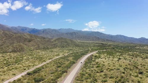 Single vehicle traveling along lonely road in desert valley with blue sky