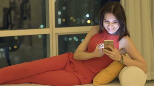 Woman Lying Down Uses Smartphone in Apartment at Night