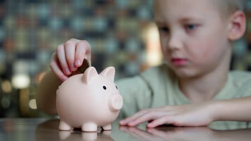 Cute serious boy putting coins into a piggy bank.