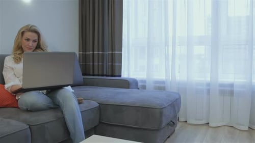 Woman Using Laptop on Gray Couch Indoors