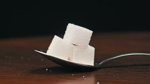 Zuckerwürfel in einem Löffel werden auf dem Tisch auf schwarzem Hintergrund gedreht. Nahaufnahme