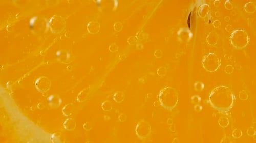 Eine Scheibe reifer Orange im Wasser sprudelt auf einem orangefarbenen Hintergrund.