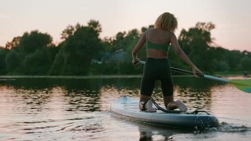 Attractive Woman Kneeling on Sup Board in Middle of Lake