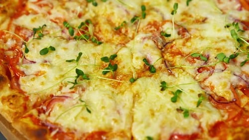 Delicious pizza. Melted cheese and green sprouts on pizza. Appetizing pizza spinning on the table.