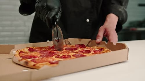 close-up man pizza chef cuts pizza lying in a delivery box with a pizza knife in the kitchen