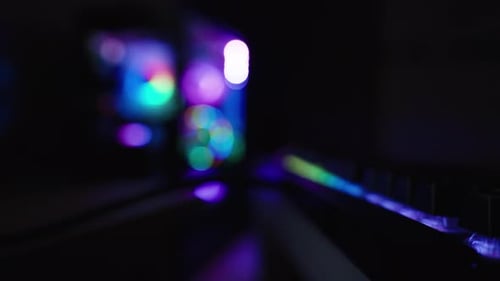 Schwarze Tastatur mit Regenbogen-Hintergrundbeleuchtung im Dunkeln und Gaming-PC dahinter mit transparenter Abdeckung und