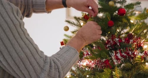 Man Decorating Christmas Tree Indoors Wearing Santa Hat